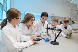 Eine Gruppe Kinder in weißen Labormänteln experimentiert in einem Labor der Montanuniversität